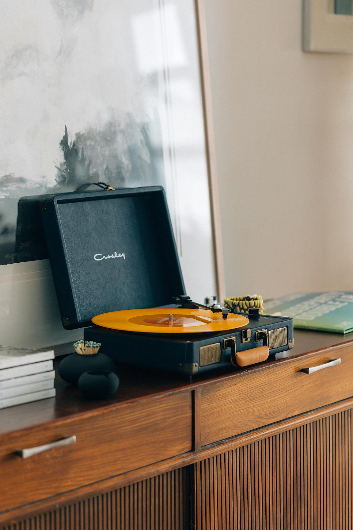 A record player plays an orange record on a wooden credenza.